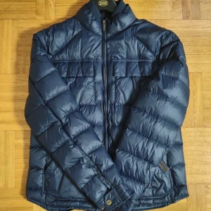 Blå Dunnjacka  - Blå Dobber jacka för män. Jackan är storlek L men passar även storlek M. Bra skick dock så finns det en liten skada på ryggen men syns inte vid användning. Hör av er vid intresse eller funderingar. PRIS KAN DISKUTERAS!