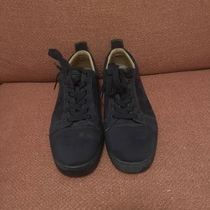 Loubs i marinblå färg utan spikar - Snygga marinblåa sneakers i mocka med rund tå och platt sula. Skorna har svarta snören och en cool röd undersida som sticker ut. Insidan är beige och de har en klassisk låg profil som passar till jeans eller shorts.