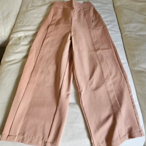 Beiga wide byxor med hög midja - Snygga beiga byxor med hög midja och breda ben. Byxorna har en rak siluett och är tillverkade i ett mjukt bomullsmaterial. Perfekta för en chill och trendig look, passar dig som gillar loose fit och stilrena färger.