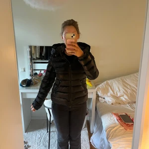 BADY DOWN JACKET Moncler - Säljer en svart bady down jacket från Moncler med huva och dragkedja. Jackan har en glansig finish, quiltad design och långa ärmar. Perfekt för kalla dagar och riktigt snygg till streetwear. Klassisk Moncler-detalj på ärmen i svart. Tyvärr defekter, vid ärmar & armhålor. Det syns knappt och påverkar ej jackans funktion. Kvitto och ärlighetsbevis medkommer! Storlek 14Y & passar mig som är en S, passar mig även när jag har hoodie/stickat under🩷hör av er vid frågor!