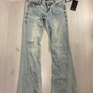 True Religion Joey Low Rise Flare Jeans - Snygga ljusblå jeans från True Religion, modell Joey Low Rise Flare. De har låg midja, utsvängda ben och coola broderade bakfickor med röd och gul detalj. De har en mörkare ”fläck” på vänster bakben som fanns när de köptes och därför är i tvätten på jeansen. De är aldrig använda.