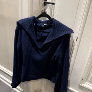 Mörkblå stickad tröja från Gina Tricot - Mysig mörkblå stickad tröja från Gina Tricot med bred, ribbad krage och lång ärm. 