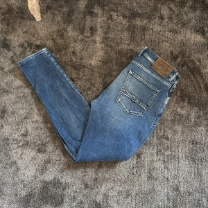 Replay blå slim jeans herr - Snygga blå jeans från Replay i modellen 511 med slim passform. Jeansen har klassisk femficksdesign, ljusa slitningar och tydliga sömmar. Perfekta för dig som gillar en smal siluett och vill ha ett par stilrena jeans i stretchigt material.