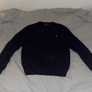 Mörkblå tröja från Polo Ralph Lauren - Säljer en mörkblå tröja från Polo Ralph Lauren i mjuk pima bomull. Tröjan har diskret vågigt mönster, rund halsringning och den klassiska broderade loggan på bröstet. Perfekt för dig som gillar stilrena och tidlösa plagg.