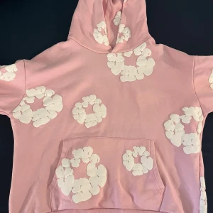 Rosa hoodie med vita blommönster - Säljer en rosa hoodie med stora vita blommönster tryckta över hela tröjan. Tröjan har huva och en klassisk magficka framtill. Perfekt för dig som gillar en söt och unik streetstyle-look.   Storlek S