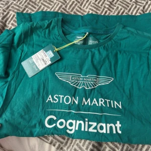 Aston Martin Cognizant t-shirt grön - Snygg grön t-shirt från Aston Martin Cognizant Formula One Team, tillverkad i mjuk bomull. Klassisk passform med rund hals och tryck framtill. Perfekt för dig som gillar motorsport, helt ny köpt i Thailand från officiellt butik 