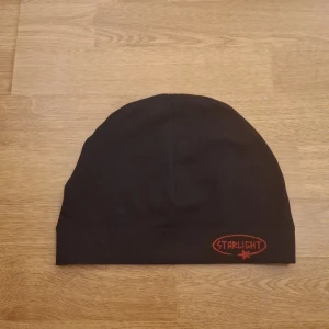 Starlight Mössa - Svart mössa från Starlight med en röd broderad logga och stjärna framtill. Enkel och clean design med uppvikt kant. Perfekt för dig som gillar streetstyle och vill ha en stilren accessoar till höst och vinter.