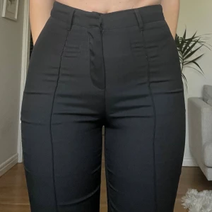 Svarta kostymbyxor med hög midja - Snygga svarta kostymbyxor med hög midja och raka ben. Byxorna har bälteshällor, diskreta sömmar framtill och stängs med dragkedja. Jättefina men har några noppror på baksida lår🩷