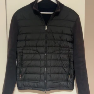 Svart cardigan från Moncler - Säljer en svart pufferjacka från Moncler med quiltad framsida och släta ärmar. Jackan har två sidofickor med dragkedja och en hög krage. Moncler-logga på vänster ärm. Perfekt för dig som vill ha en stilren och varm jacka.  Dm för mer bilder 