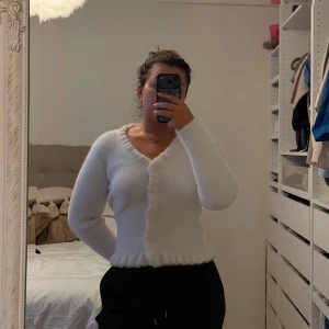 Vit fluffig kofta med v-ringning - Supermjuk och fluffig vit kofta med v-ringning och knappar framtill. Koftan har lång ärm och ribbad kant nedtill för en snygg passform. Perfekt för lager-på-lager och ger en cozy vibe till din outfit.