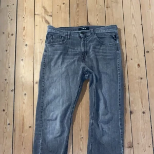 Replay grå jeans straight fit - Snygga grå jeans från Replay med klassisk femficksdesign och raka ben. Modellen heter Thad och har en normal passform. Jeansen är tillverkade i slitstarkt denim och har subtila slitningar för en cool look. Perfekt för dig som gillar stilrena och tidlösa jeans. Storlek 29/32 (är rätt tajta i midjan pga modell) 