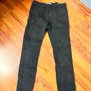 Svarta chinos från H&M L.O.G.G. - Svarta chinos från H&M L.O.G.G. i storlek W30. Byxorna har klassisk passform med snedställda fickor fram och bälteshällor. Tillverkade i bomull för en skön känsla och stilren look. Perfekta för dig som gillar enkel och clean stil.