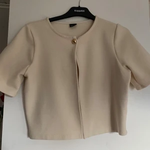 Beige kofta - Beige kofta från Gina tricot, storlek S. Koftan har en enkel design med en dekorativ guldig knapp framtill och är croppad i modellen. 