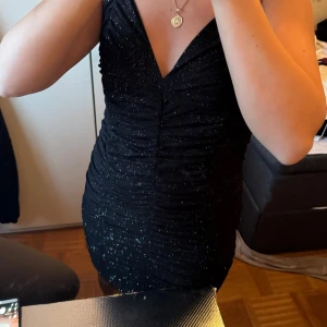 Svart glittrig kort klänning - Supersnygg svart glittrig klänning med smala axelband och djup v-ringning. Tight passform och rynkade detaljer längs hela klänningen ger en riktigt snygg siluett. Perfekt för dig som vill sticka ut med lite extra glitter. Köpte för 1500 kronor på zalando