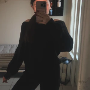 Svart offshoulder stickad tröja - Säljer en svart stickad tröja med offshoulder-modell och långa ärmar. Tröjan har en loose passform och bred krage som sitter snyggt över axlarna. Perfekt för dig som gillar en chill och trendig look.