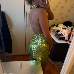 Grön glittrig paljettklänning - Säljer en superglittrig grön paljettklänning med halterneck och öppen rygg. Klänningen är kort och tight, perfekt för dig som vill sticka ut. Den har en snygg passform och är täckt av glittrande paljetter som fångar ljuset.från Gina tricot 