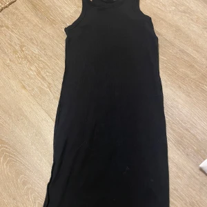 Svart ärmlös långklänning S - En stilren svart långklänning i ärmlös modell med rund halsringning. Klänningen har en rak passform och är tillverkad i ett mjukt, stretchigt material som känns bekvämt mot huden. Perfekt för dig som gillar minimalistisk och clean stil.