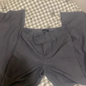 Grå kostymbyxor från Gina Tricot - Snygga grå kostymbyxor från Gina Tricot i storlek 34. Byxorna har mid midja, utsvänga . Helt nya och inte använd.