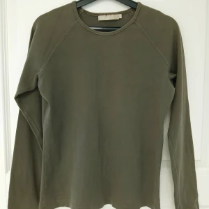Långärmad tröja med raglanärmar - En stilren grön långärmad tröja med rund halsringning och raglanärmar. Tillverkad i bomull. Perfekt att bära för en chill look. Tröjan har naturligtvis tvättats. Se bilder för skick och passform. Storlek 42/44 enligt lappen men då måttet armhåla till armhåla är cirka 48 cm så stämmer 42 bättre. Axelsöm till ärmslut är cirka 68 cm. Tvättas i 40 grader.