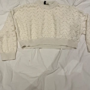 Vit croppad stickad tröja - Säljer en vit croppad stickad tröja med snyggt hålmönster och ribbade muddar vid ärmslut och nederkant. Tröjan har lång ärm och en rundad halsringning, perfekt för dig som gillar en chill och trendig look.