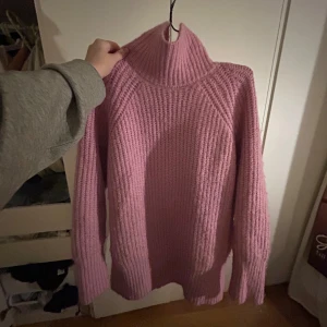 Rosa stickad polotröja - Mysig stor rosa stickad polotröja med grov ribbstickning och höga muddar. Tröjan har lång ärm och en hög polokrage som ger extra värme. Perfekt för kyliga dagar och enkel att styla med jeans eller kjol.