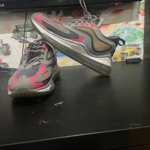 Nike Air Max 720 sneakers grå/rosa - Nike Air Max 720 sneakers med futuristisk design i grått, svart och rosa. Skorna har en tjock genomskinlig sula, mesh och syntetdetaljer samt snörning. Perfekta för dig som gillar streetstyle och vill sticka ut med färg och form.