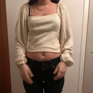 Krämvit blus med puffärmar - Säljer en krämvit blus med fyrkantig halsringning och långa puffärmar. Toppen är croppad och har ett smockat, ribbat tyg som ger en snygg struktur. 🥰🥰