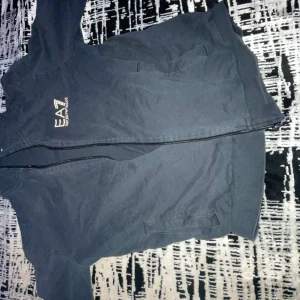 Svart zipper från EA7 Emporio Armani - Säljer en svart zipper från EA7 Emporio Armani med stilren logga på bröstet. Jackan har dragkedja framtill och två sidofickor. Perfekt för dig som gillar sportig och clean stil.
