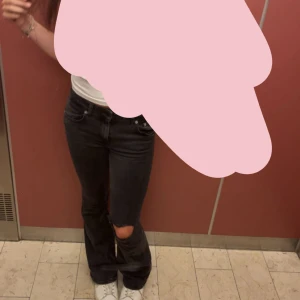 Svarta bootcut jeans med hål - Snygga svarta jeans med bootcut passform och ett stort hål vid ena knät. Klassisk femficksmodell och normal midja. Perfekta för dig som gillar en avslappnad och trendig stil.