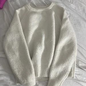 Vit stickad tröja med ribbade muddar - Säljer en vit stickad tröja med rund hals och ribbade muddar vid ärmslut och nederkant. Tröjan har en enkel och clean look, perfekt för dig som gillar minimalistisk stil. Långärmad och mjuk, passar när du vill vara extra cozy.