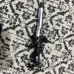 Coline Locktång - Elektrisk locktång från Coline med svart handtag och blankt metallrör. Sladden är intakt och produkten ser ut att vara i gott begagnat skick utan synliga defekter. Perfekt för att skapa snygga lockar hemma. Enkel att använda och passar de flesta hårtyper.