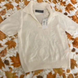 Ivory pikétröja från Primark - Snygg ivoryfärgad pikétröja från Primark i storlek 2XS. Tröjan har klassisk krage, korta ärmar och är stickad i mjukt material. Perfekt för dig som gillar en clean och fräsch look med lite retrovibe. Passar dig som vill ha en enkel men stilren topp.