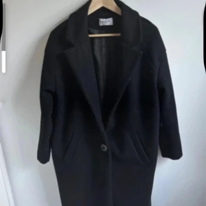 Svart oversized kappa från Yu & Me Paris - Säljer en svart kappa från Yu & Me Paris med klassisk krage och enkel knappstängning framtill. Jackan har lång ärm, två fickor och är tillverkad i ett ulligt material som känns både stilrent och chill. Perfekt för dig som gillar minimalistisk vibe. Den har lite ytludd.