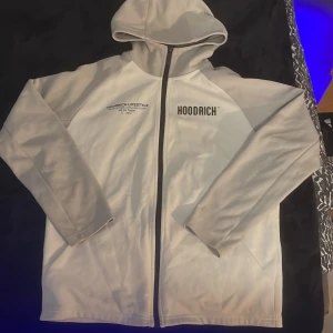 Vit hoodie från Hoodrich med tryck - Säljer en vit hoodie från Hoodrich i storlek XS. Tröjan har svart dragkedja, huva och tryck både fram och bak med texten 'HOODRICH LIFESTYLE' och 'WORLDWIDE ORGANISATION'. Perfekt för dig som gillar streetwear. OBS passar S jättebra nypris 850