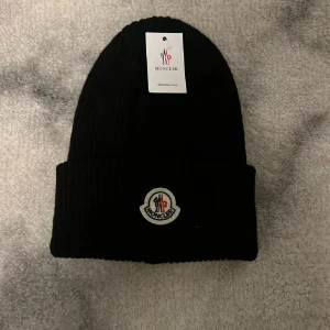 Svart Moncler mössa i ribbstickad ull - Svart Moncler mössa. Lapp medföljer. Oanvänd. 
