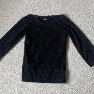 Svart spetsblus från Kappahl - Svart blus från Kappahl med trekvartsärm i genombruten spets och vacker spetskant vid halsringningen. Framsidan är helspets medan baksidan är i mjuk bomull. Perfekt för dig som gillar romantiska detaljer.