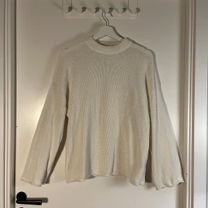 Vit stickad tröja från Junkyard - Vit stickad tröja från Junkyard med rund hals och avslappnad passform. Tröjan har långa ärmar och är tillverkad av 65% återvunnen polyester och 35% återvunnen bomull. Perfekt för dig som gillar enkel och clean stil.