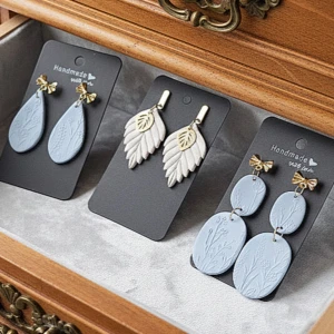 3 par handgjorda örhängen med "Isblå toner" - Tre par unika örhängen: två i ljusblått med ingraverade blommor och små guldfärgade rosetter, samt ett par vita örhängen i form av blad med gulddetaljer. Perfekta för dig som vill sticka ut med stilrena och kreativa accessoarer.