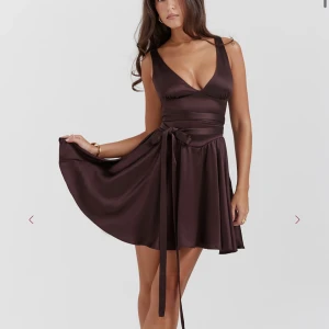 Brun omlottklänning i satin House of CB - Supersnygg brun kort omlottklänning i satin med djup v-ringning och breda axelband. Klänningen har ett markerat midjeband som knyts i sidan och ger en riktigt smickrande siluett. Perfekt för dig som vill sticka ut med en elegant och trendig look. Originalpris: 2200kr. Finns inte längre att köpa på hemsidan 