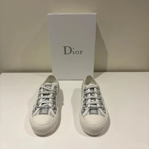 Dior sneakers  - Snygga Dior sneakers i vitt och grått med klassiskt Dior-monogram över hela skon. Modellen har rund tå, platt sula och snörning framtill. Nypris är runt 9000kr! Använd få gånger. Hör av er vid frågor💘💘