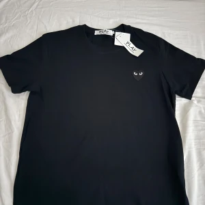 Svart t-shirt Commes des Garçons Play - Svart t-shirt från Commes des Garçons Play med klassiskt hjärta med ögon broderat på bröstet. T-shirten har rund hals, korta ärmar och är gjord i mjuk bomull. En clean och stilren tee med ikonisk detalj, perfekt till jeans eller shorts.