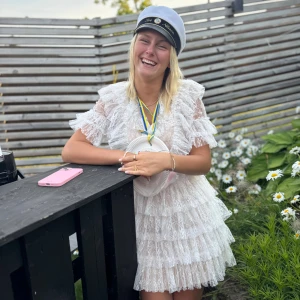 Vit spetsklänning/studentklänning med volanger - Superfin vit kort spetsklänning med flera lager volanger och v-ringad hals. Klänningen är ärmlös med transparent spets. Perfekt för student eller sommarens alla tillfällen. Säljer då jag inte längre använder den! Har bara använt en gång! 