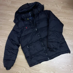 Polo Ralph Lauren - 🧥 Polo Ralph Lauren dunjacka – storlek M Snygg och varm jacka från Polo Ralph Lauren i svart färg. Jackan har huva (avtagbar) och dragkedja med “RL”-detalj. I mycket bra skick – inga fläckar eller skador. Storlek: M Lätt men väldigt varm, perfekt för höst och vinter ❄️🔥