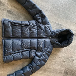 Mörkblå dunjacka Peak Performance S - Säljer en mörkblå dunjacka från Peak Performance, modell W Frost Down Jacket. Jackan har huva, dragkedja framtill och quiltad design. Nypris 4200kr. Perfekt för kalla dagar med sin fluffiga och stilrena look. Passar dig som gillar sportig och clean stil.