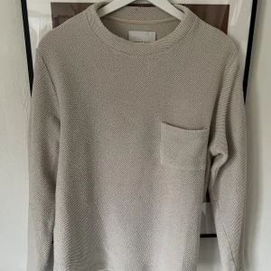 Beige stickad tröja Samsøe Samsøe - Snygg beige stickad tröja från Samsøe Samsøe med rund halsringning och en bröstficka. Tröjan har en grovstickad struktur och långa ärmar, perfekt för lager-på-lager. Enkel och stilren design som passar till allt.