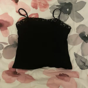 Svart linnetopp med spetskant - Säljer en svart linnetopp med smala axelband och snygg spetskant upptill. 