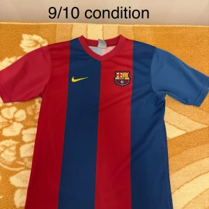 FC Barcelona Nike fotbollströja XL kids / S Men  - Klassisk FC Barcelona fotbollströja från Nike i storlek XL. Tröjan har breda vertikala ränder i rött och marinblått, gul Nike-logga och broderat klubbmärke på bröstet. Tillverkad i lätt och ventilerande polyester, perfekt för match eller träning.