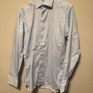 Ljusblå slim fit skjorta från Eton - Snygg ljusblå skjorta från Eton i slim fit-modell. Skjortan har klassisk krage, långa ärmar med manschett och knappar framtill. Tillverkad i mjuk bomull som känns skön mot huden. Perfekt för dig som gillar stilrena och fräscha plagg.