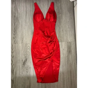 Röd satinklänning - Snygg röd klänning i satin med djup v-ringning och breda axelband samt inbyggda kupor. Figurnära passform och omlott-detalj framtill som skapar en slits. Använd en gång, i utmärkt skick ❤️