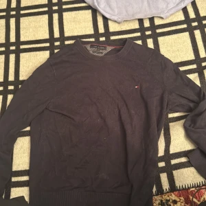 Mörkblå stickad tröja Tommy Hilfiger - Snygg mörkblå stickad tröja från Tommy Hilfiger med rund halsringning och diskret logga på bröstet. Tröjan är i bomullskashmir-blandning och har ribbade muddar vid ärmslut och nederkant. Perfekt för lager-på-lager under hösten och vintern.